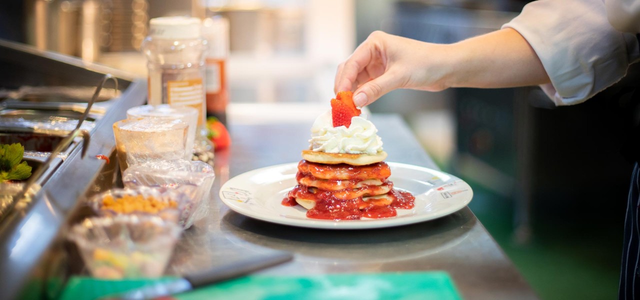 A chef putting a strawberry on top of a stack of pancakes in a kitchen 
