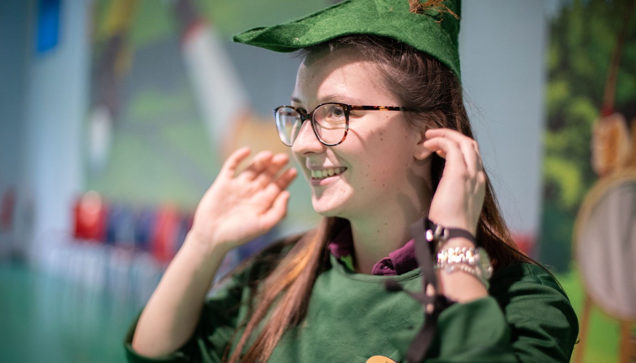 Member of staff from the Activity Den wearing  a Robin Hood style hat and smiling