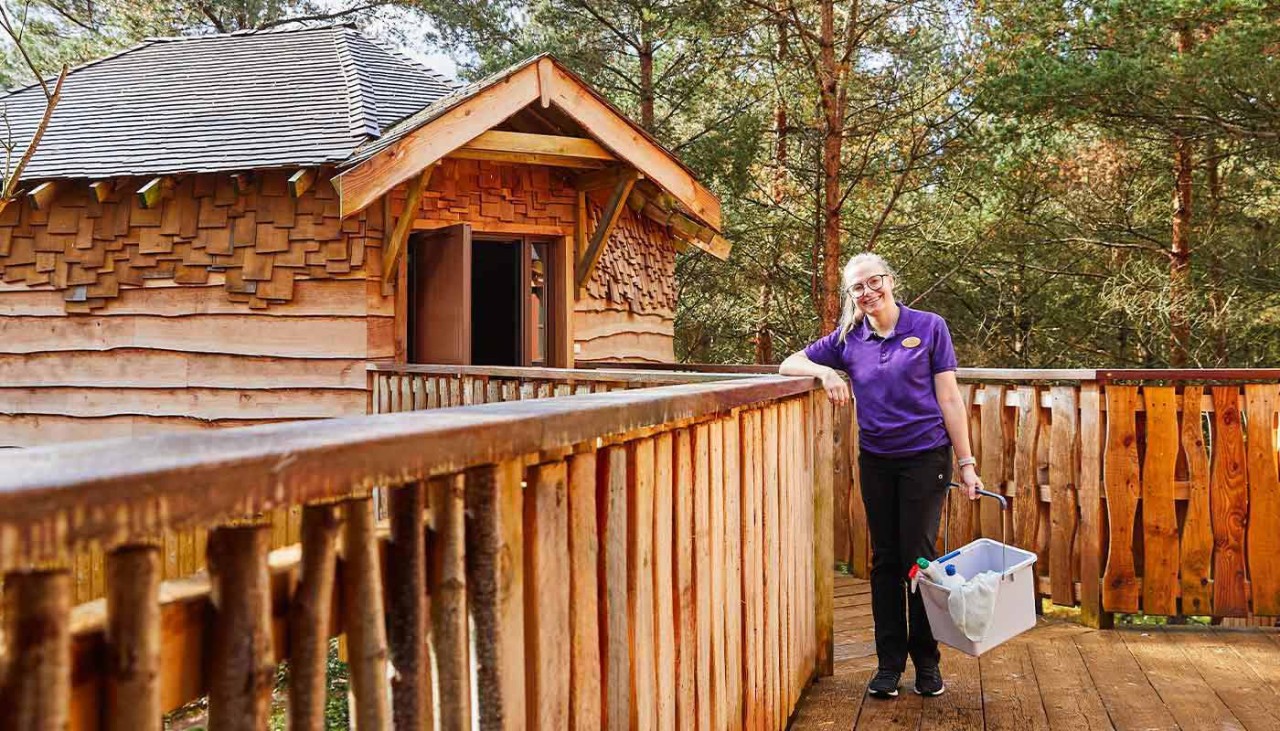 Member of staff stood with a cleaning bucket on the balcony of a treehouse 