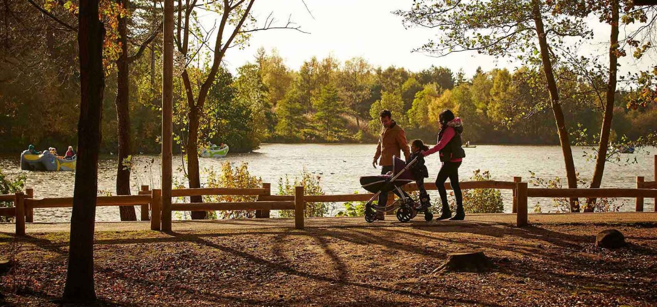 Family walking past the lake holding hands and pushing a pram