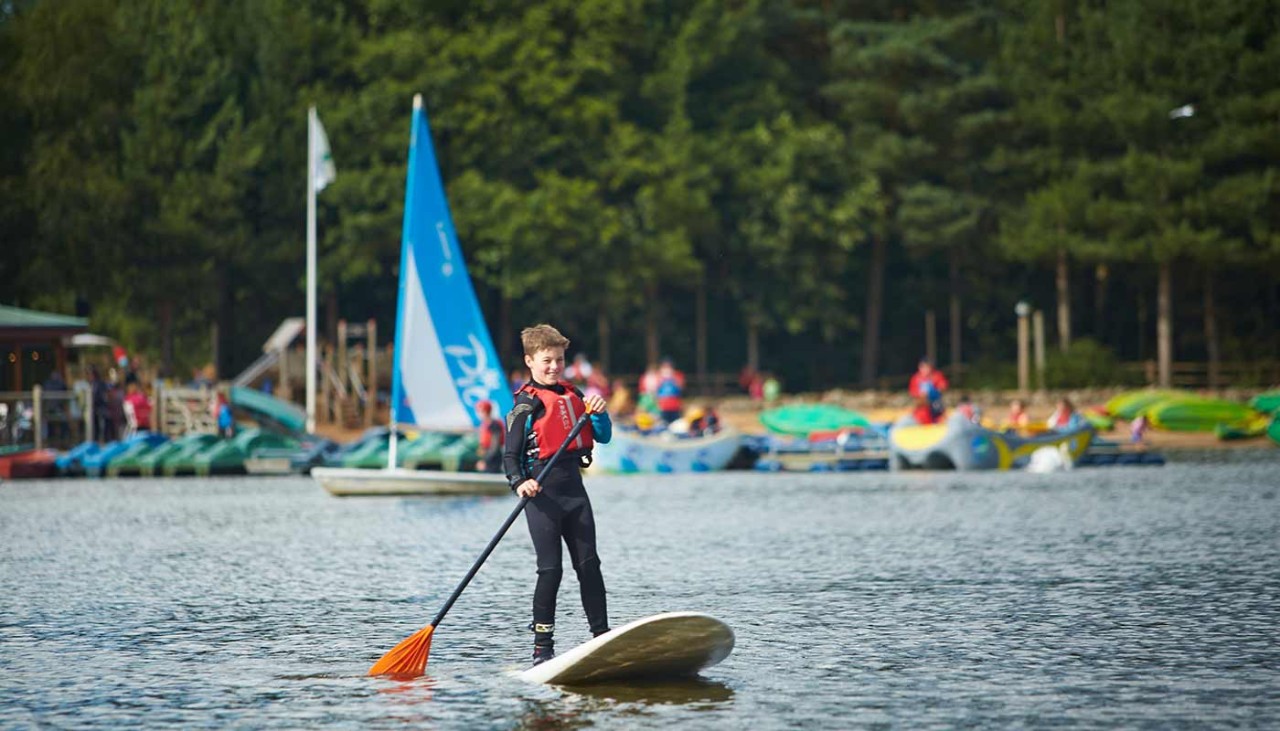 A child wearing a life jacket paddleboarding on the lake 