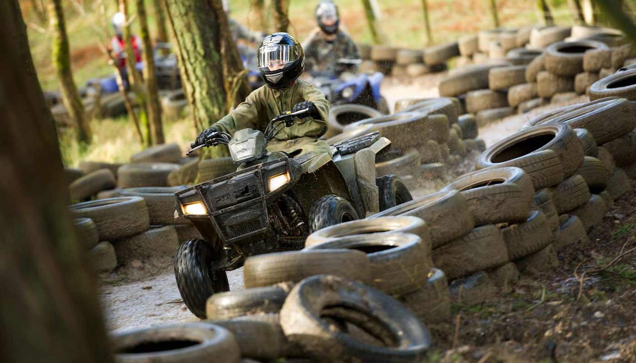 A child wearing protective gear and riding a quad bike around a track made of stacked up tires