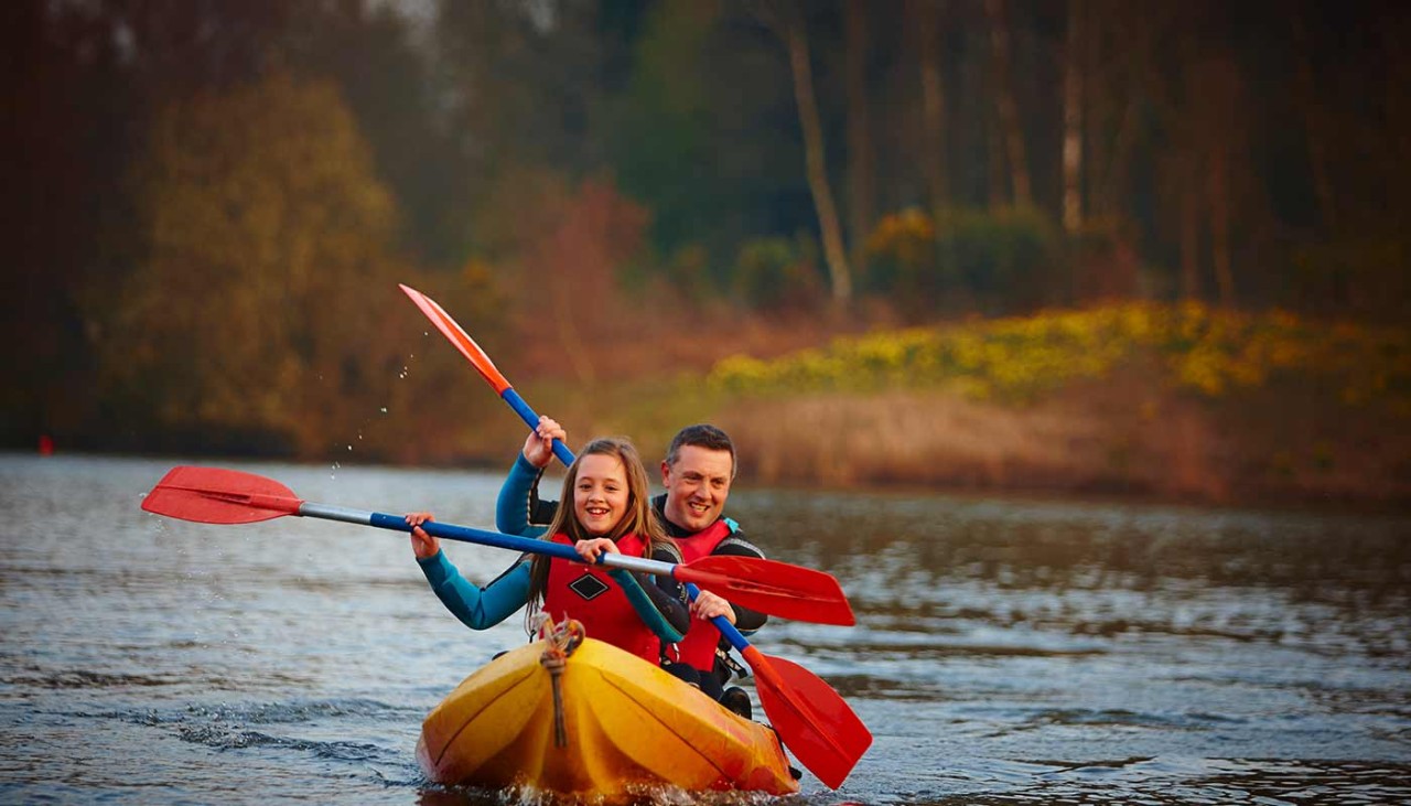 A father and daughter in a bright yellow kayak on the lake