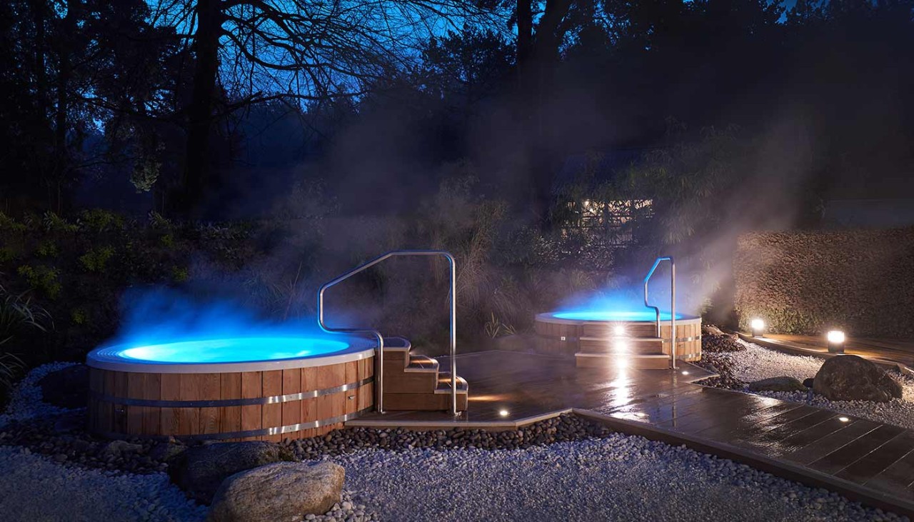 Two hot tubs outside the Aqua Sana with steam rising from them and  blue light shining from them