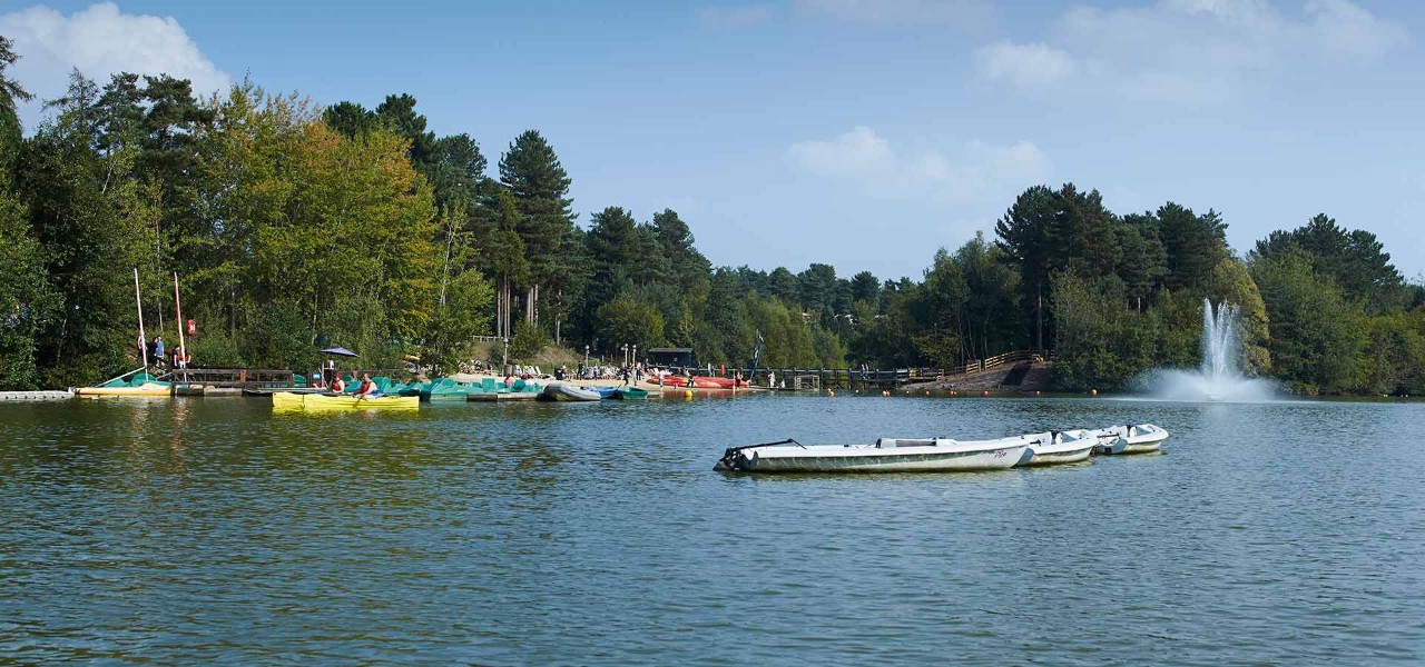 Elveden Lake with boats on it and water fountain and forest in the distance 
