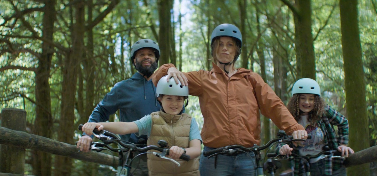 Family on bikes wearing helmets, looking directly into the camera smiling