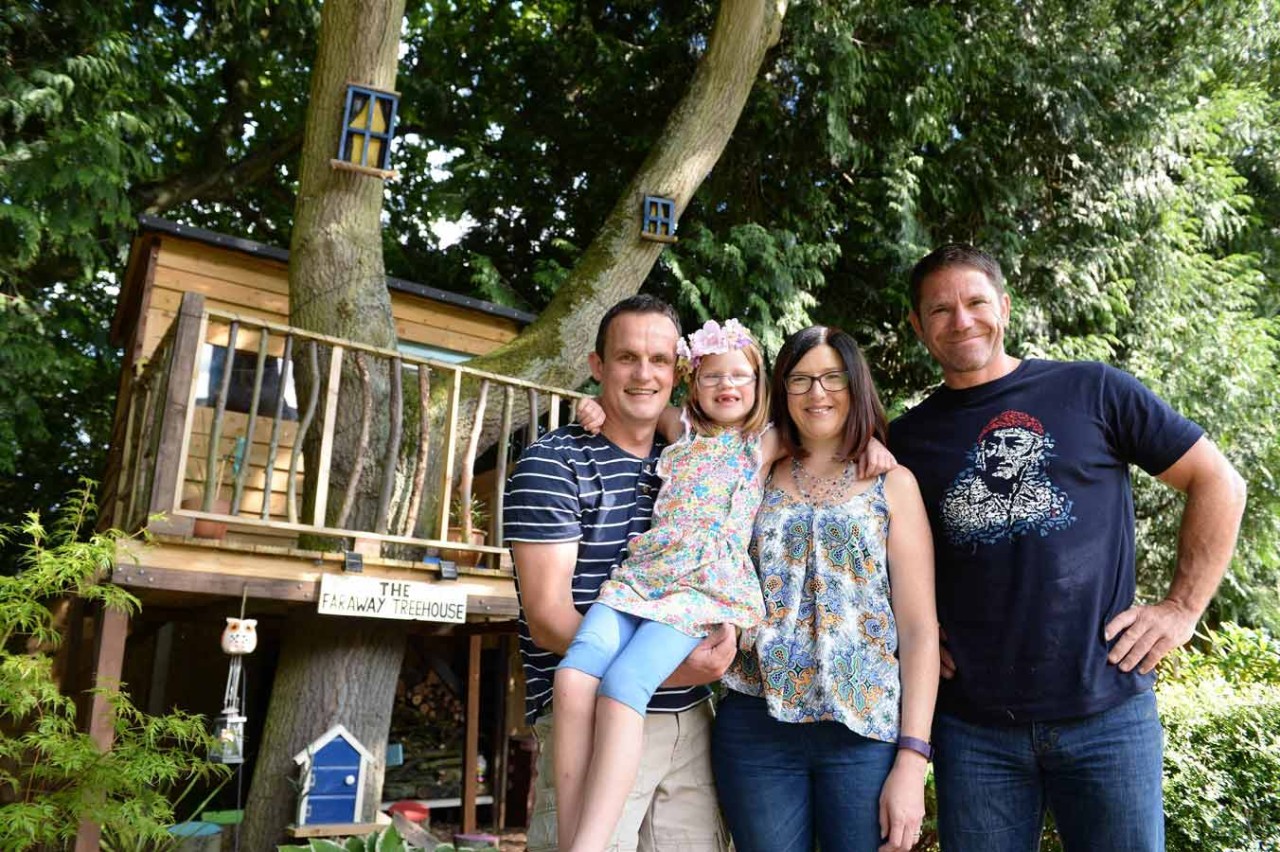 Family standing next to a treehouse they have built in their garden
