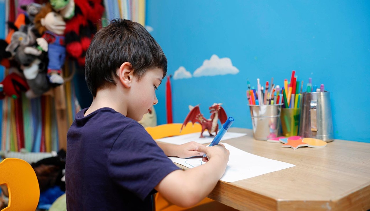 A young boy drawing on a piece of paper at a desk