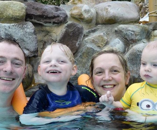 A family swimming in the pool smiling at camera 