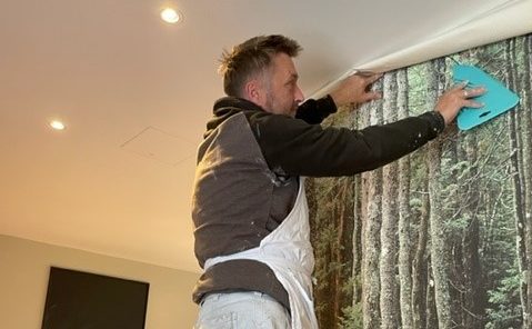 A man in an apron putting up wallpaper in a lodge
