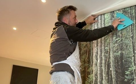 A man in an apron putting up wallpaper in a lodge